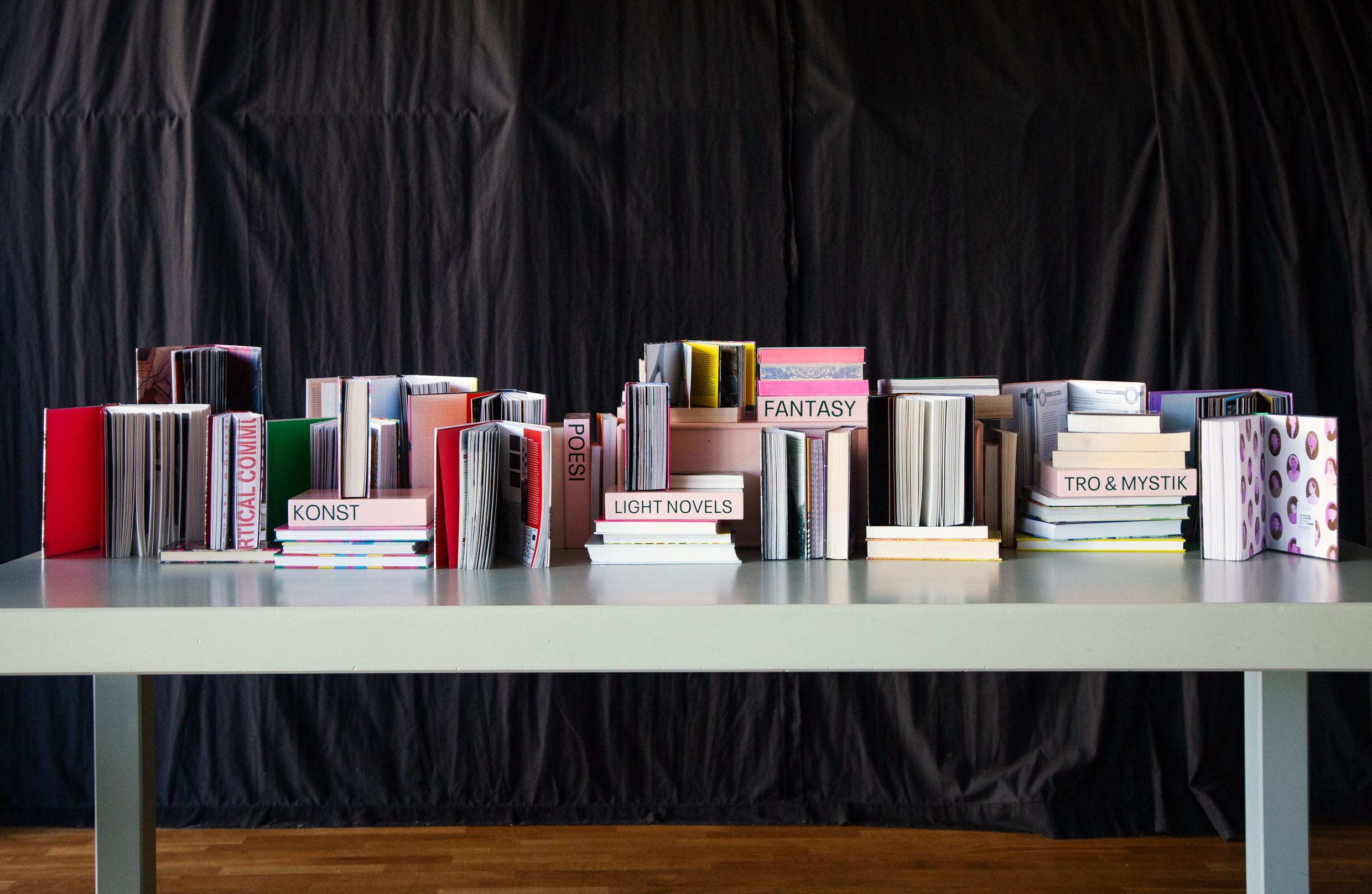 Bord med uppställda böcker i olika genrer som "Konst", "Fantasy" och "Poesi".