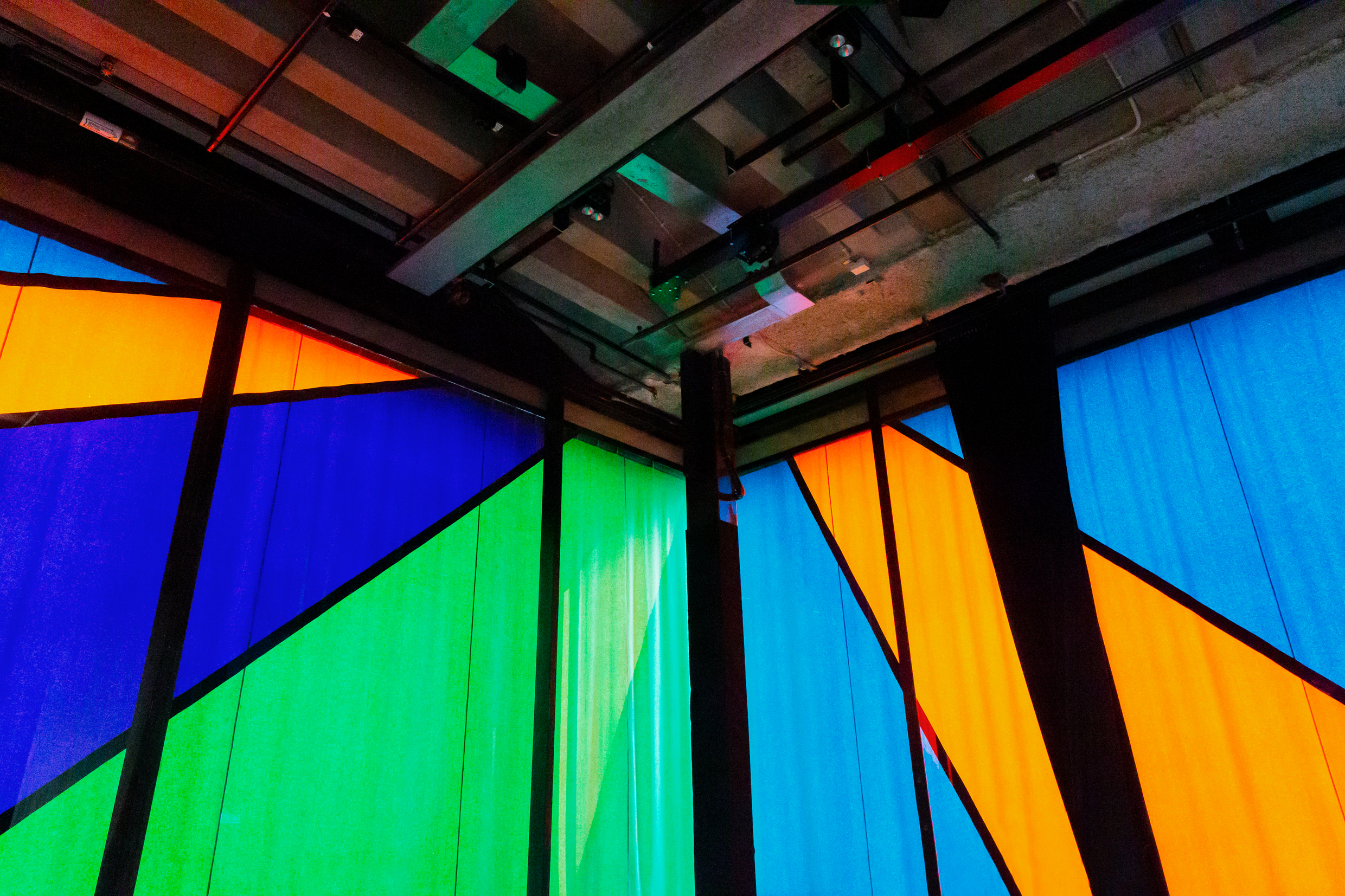 Färgstarka paneler i blått, grönt och orange bildar geometriska mönster i Hörsalen på Kulturhuset Stadsteatern, med synliga takbjälkar och industriell estetik. Konstverk av Olle Bærtling.