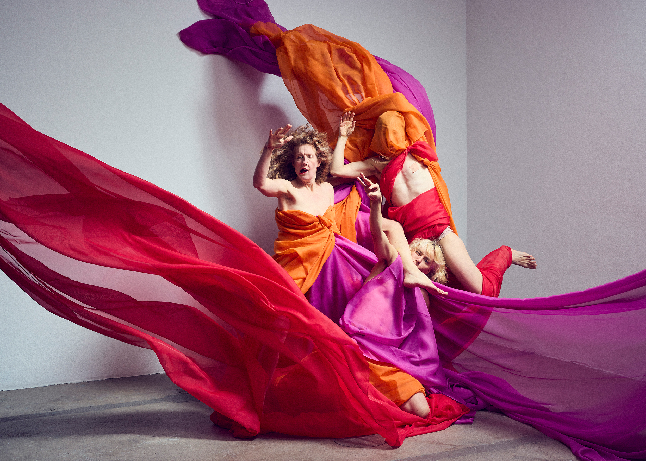 Det blåser och tre kvinnor trasslar in sig i färgglada tyger.