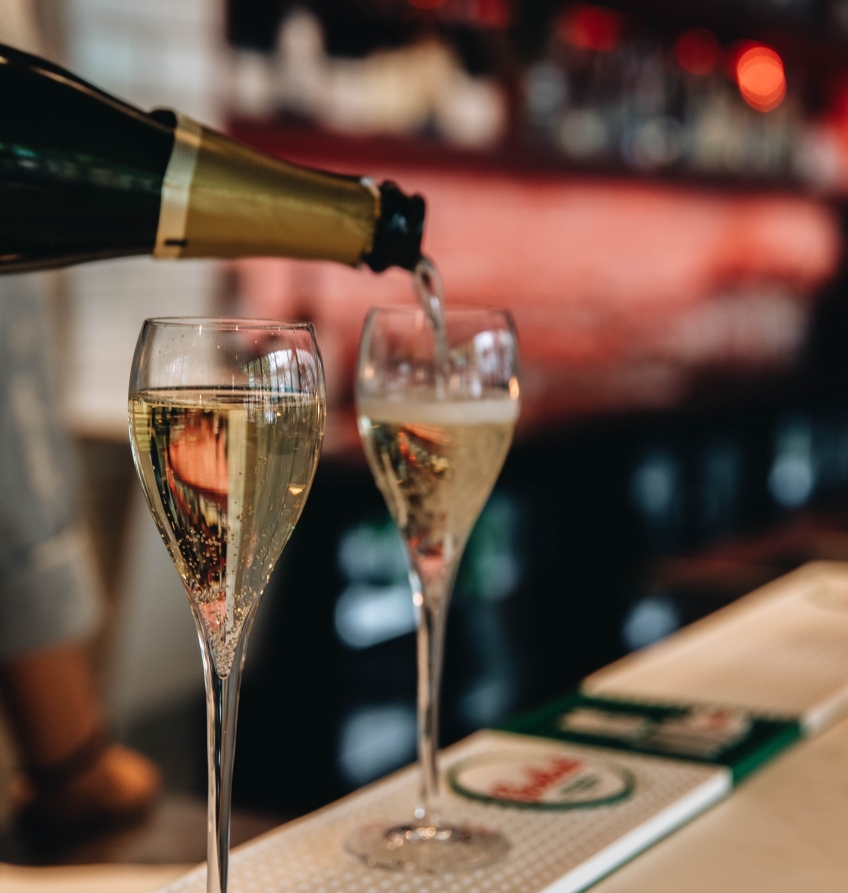 Två champagneglas på en bardisk fylls på med champagne. 