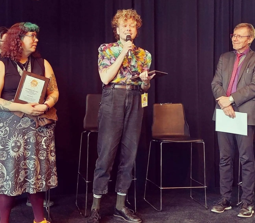 En glad person på en scen tar emot ett pris. 