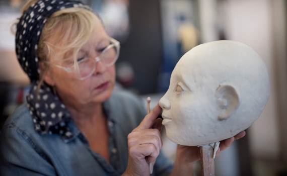 En dockmakare arbetar med huvudet på en docka. 