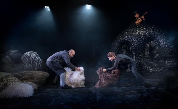 Två skådespelare på scen som håller i varsitt stort pälsstycke. 