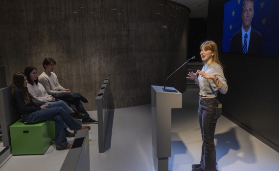 En ungdom står vid en talarstol, framför sitter andra ungdomar och lyssnar. 