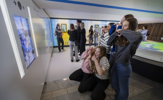 Ungdomar formar mönster med sina händer framför en tv-skärm. 