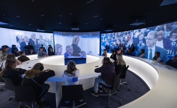 Ungdomar kring ett runt bord, runtom dem är det stora tv-skärmar.