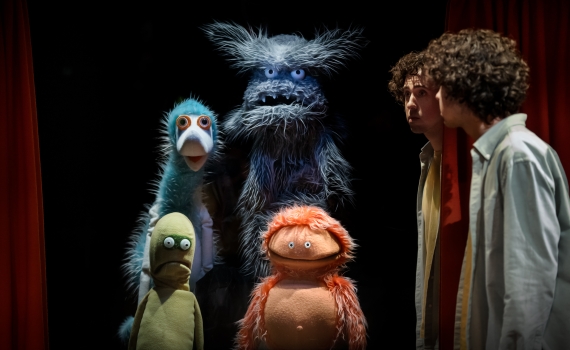 Fyra lurviga dockor i olika storlekar, tillsammans med två människor, på en scen.