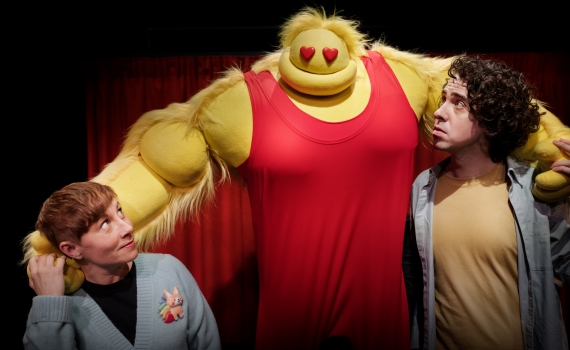 En stor gul docka håller armarna om två personer. 