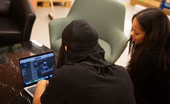 Två personer sitter framför ett musikredigeringsprogram vid en dator. 