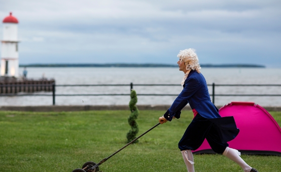 En tjänare i 1700-talskläder som klipper gräset