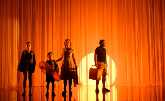 Fyra personer, två vuxna och två barn, står framför orange bakgrundsbelysning med badutrustning i händerna.