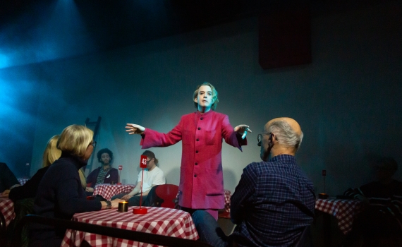 Andreas T Olsson som Dante, han står mellan bord där det sitter människor.