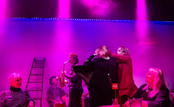 Andreas T Olsson som Dante i en dans och Axel Mårdsjö som Casella som spelar saxofon. Rummet är fullt med människor.