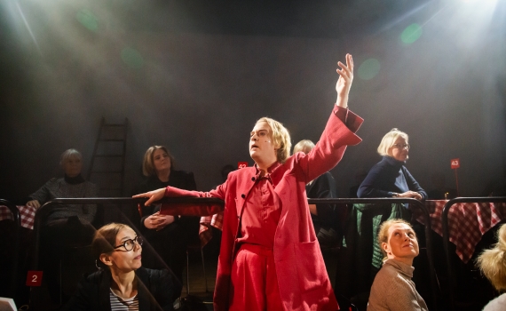 Andreas T Olsson som Dante, han lutar sig mot ett räcke och sträcker ut sin hand. Rummet är fullt av människor. 