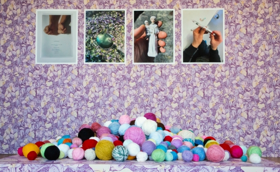 Färgglada garnbollar ligger framför fyra foton på en lila blommig väggtapet.