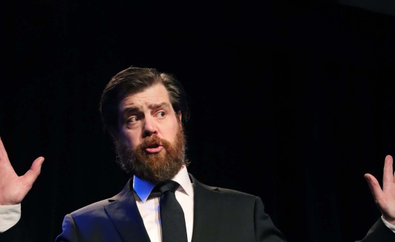 En man i svart kostym och svart slips som sträcker upp sina händer i luften.