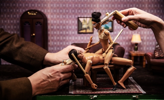 Två nakna dockor i samlagsliknande position styrs av flera vuxna händer i ett dockrum.