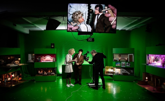 Tre vuxna i green screen-studio filmar och manipulerar dockor, bild från scenen visas på skärm ovan.