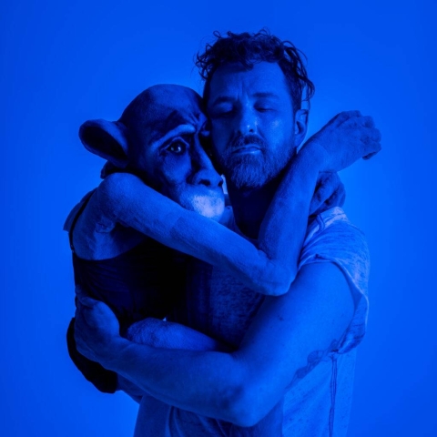 En man håller om en stor docka som ser ut som en apa. 