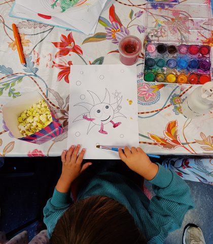 Ett barn målar och äter popcorn.