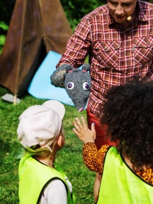 En skådespelare visar en handdocka för två nyfikna barn. 
