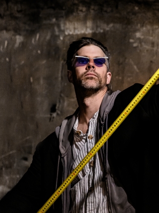 En man i solglasögon håller i ett långt gult måttband. 