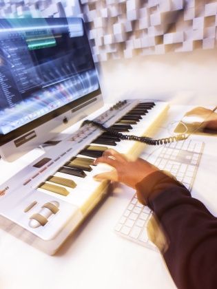 En person sitter vid en dator och jobbar med ett ljudredigeringsprogram.