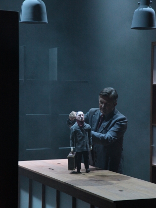 En man i grå kostym håller i en docka i grå kostym. 