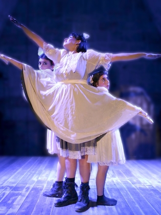 Tre personer i vita klänningar, där en hoppar högt i ett danssteg. 