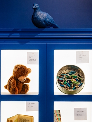 Ett blått skåp med bilder på en nalle, färgkritor, en bok med mera. 