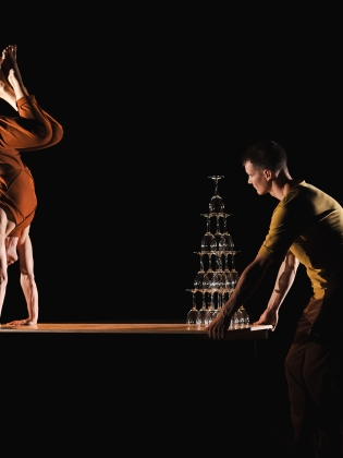 En person står på händer på ett bord med vinglas på. 