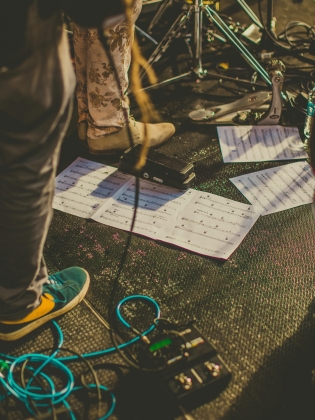 Ett scengolv fullt av kablar, papper med noter, ställningar för olika instrument med mera. 