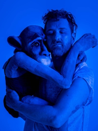 En man håller om en stor docka som ser ut som en apa. 