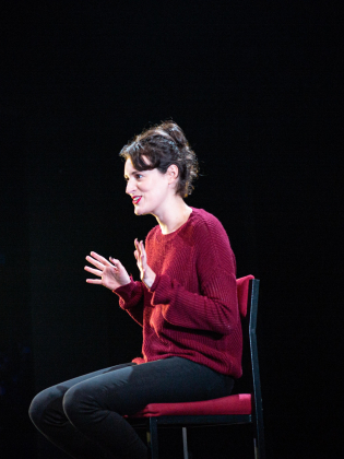 En kvinna i röd tröja framträder på en scen.