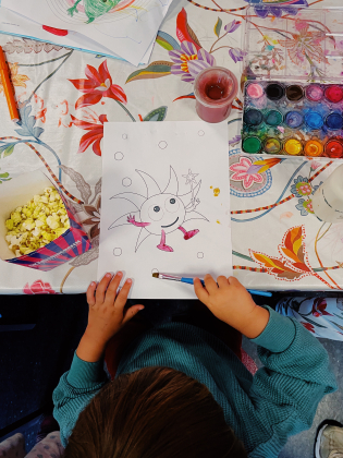 Ett barn målar och äter popcorn.