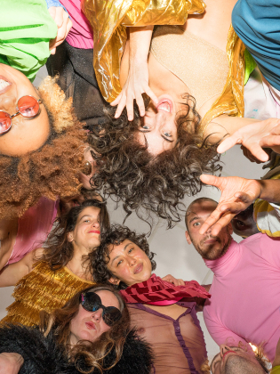 En grupp människor i färgstarka kläder, samlade i en cirkel och tittar in i kameran, skapar en känsla av gemenskap och glädje.