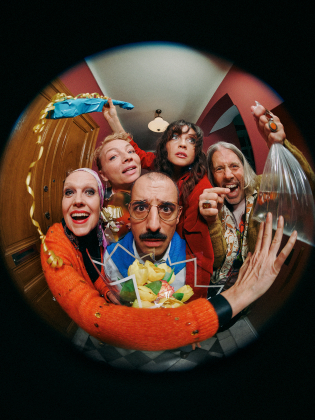 En grupp glada och förväntansfulla karaktärer, sedda genom ett fiskögeperspektiv, redo att överraska med ett paket och livfulla uttryck.