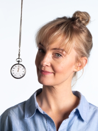 Sofia Pekkari med ett leende och lätt vridet huvud. Bredvid henne hänger ett silvrigt fickur