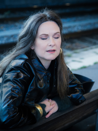 En kvinna sitter på en bänk vid ett järnvägsspår och blundar