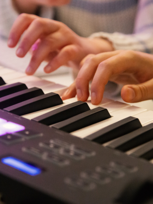 Två personer spelar på ett digitalt piano, med fokus på deras händer på tangenterna.