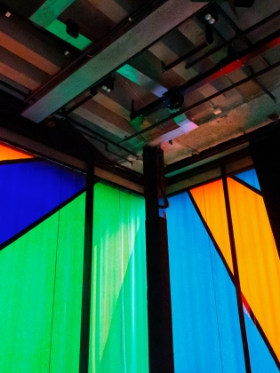 Färgstarka paneler i blått, grönt och orange bildar geometriska mönster i Hörsalen på Kulturhuset Stadsteatern, med synliga takbjälkar och industriell estetik. Konstverk av Olle Bærtling.