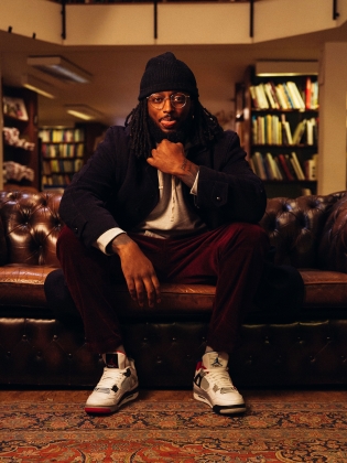 Ahmed Berhan fotad i en biblioteksmiljö. Han sitter på en bänk och räcker ut tungan