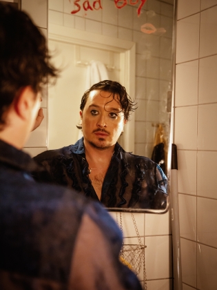 Richard Hamrin i ett badrum tittandes in i en spegel där det står sad boy skrivet på glaset