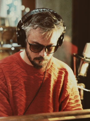 Foto föreställande man i i hörlurar, solglasögon och orange tröja