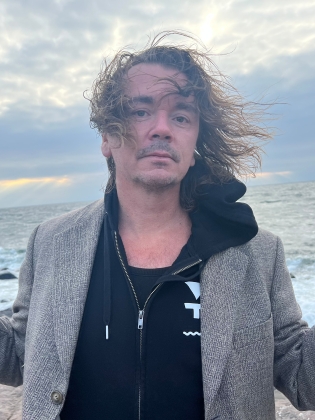 En man i kavaj och huvtröja på en strand