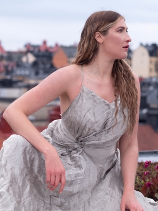 Operasångaren Maja Frydén i en grå klänning sittandes på ett tak