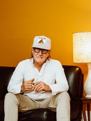 En man klädd i vitt sitter i en soffa framför en gul vägg