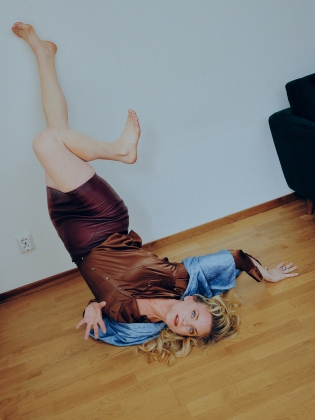 Kvinna i 30–40-årsåldern ligger på golvet med benen upp mot väggen, iklädd brun klänning med blå detaljer.