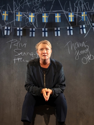 En kvinna sitter på en pall, bakom henne hänger svenska och finska flaggor