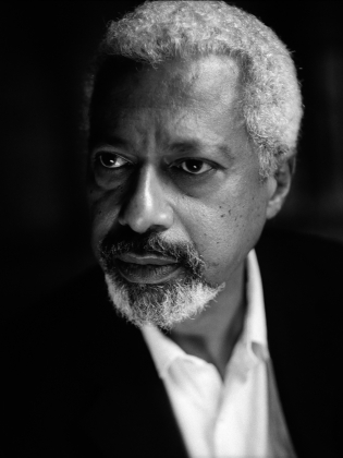 Äldre man med grått hår och skägg i kavaj och skjorta, fotograferad i svartvitt porträtt.